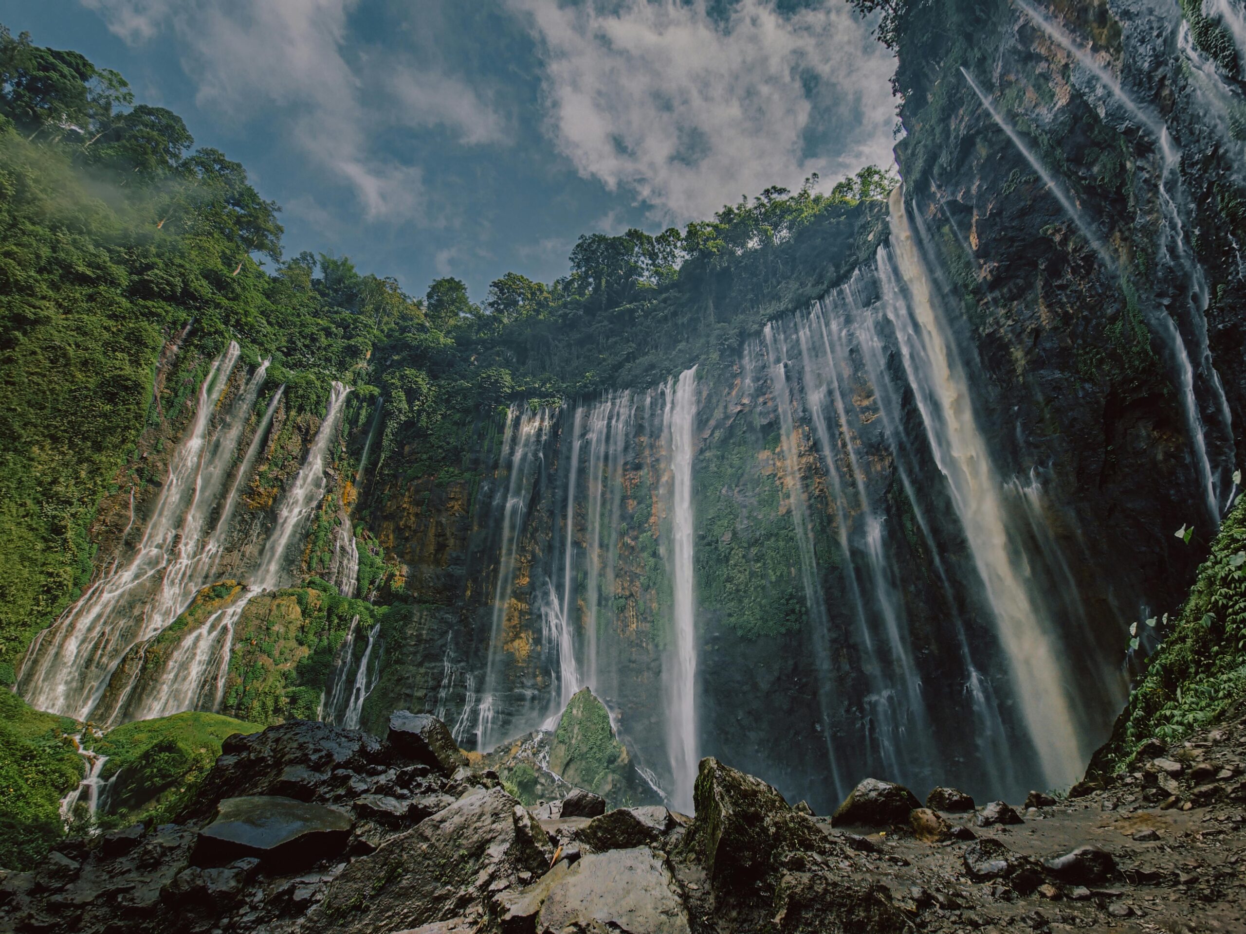 Breathtaking view of a majestic waterfall cascading through a vibrant green forest under a bright blue sky.